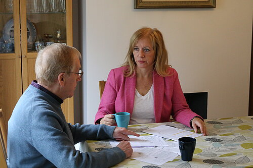 Liz speaking to man sat at kitchen table