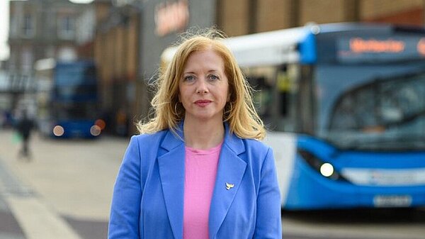 Liz Jarvis stands in front of blue bus