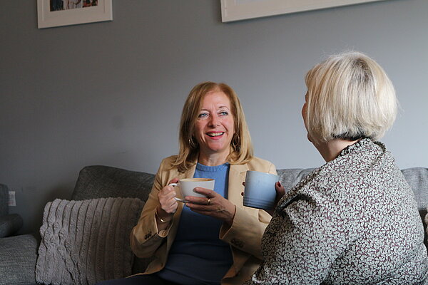 Liz speaking to woman sitting on sofa with cup